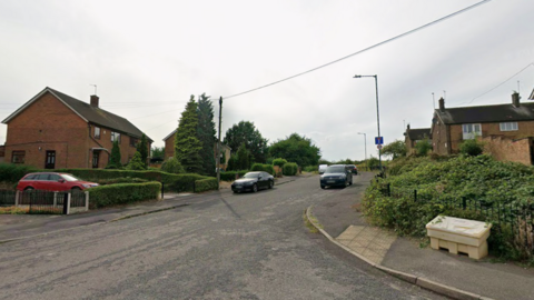 A Google streetview of a cul-de-sac with cars parked on both sides and houses.

