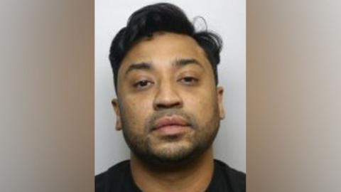 A police mugshot of Shafiqul Islam Ali. He has dark hair and stubble and is wearing a black jumper.