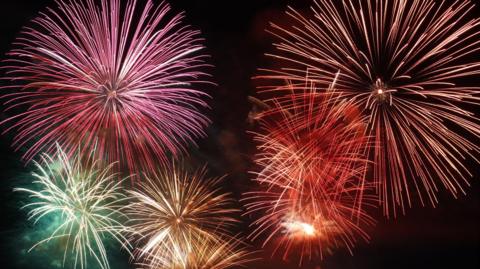 Big multi-coloured fireworks, all at the point of explosion, a pink one in the left, red in the right and green in the bottom left. 