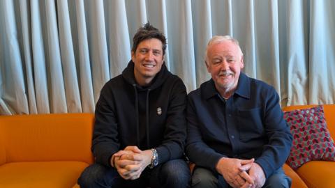 Vernon Kay (left) and Les Dennis (right) sitting on an orange couch
