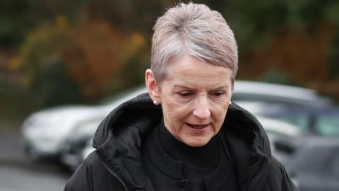 A close-up image of Lady Eleanor Donaldson as she walks out of court. She is an older woman with short, grey hair and is looking down. She is wearing a black, puffer raincoat and a pair of silver stud earrings.
