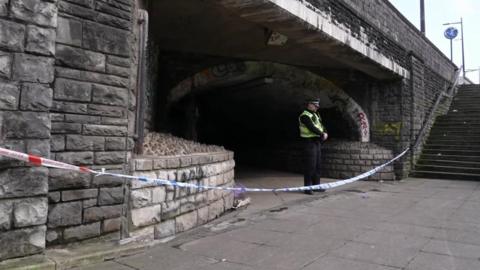 Police officer standing in an underground passageway with a police tapes across it