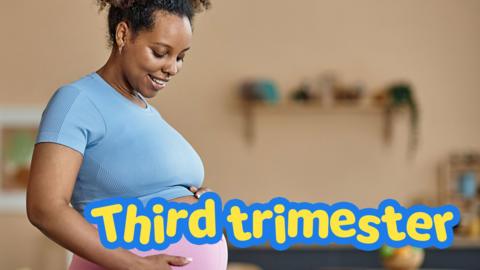 A woman in stretchy trousers holds her bump.