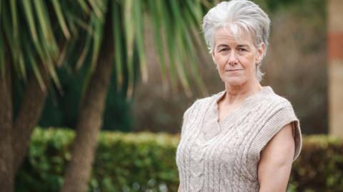 Jill Owen in a beige top standing in a garden