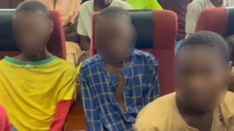 Three young men sit a Nigerian court, two wear yellow tops and one wears a blue shirt. Their faces have been blurred to protect their identities.