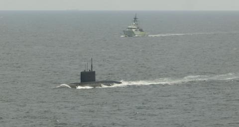 A submarine at the front of the image in the water with HMS Mersey in the distance