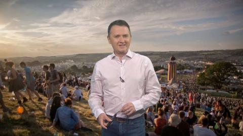 Matt standing in front of a picture of people on Glastonbury field