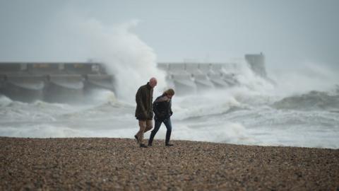 View of two people braced against the wind on the beach at Brighton marina, East Sussex