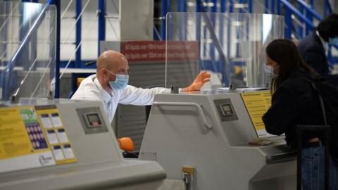 Ground staff attend to a customer at a check-in desk at Manchester Airport, while wearing a face mask