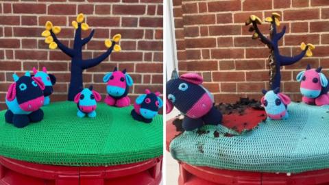 A side by side picture of the topper before and after being destroyed. The original version has a green base with four knitted cows, which are pink and blue. Behind them is a large knitted tree with orange leaves. The destroyed version is half missing and most is marked by black burns.