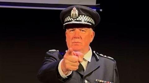 Man wearing a police chief's uniform points at the camera