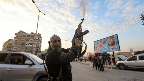 A Syrian rebel fighter fires into the air in the city of Hama, Syria (5 December 2024)