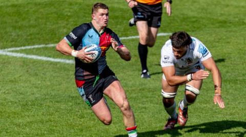 Ben Waghorn breaks forward, holding the ball in one hand as an Exeter player stumbles to try and catch him