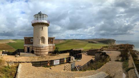 A cream lighthouse sits at the top of a cliff.