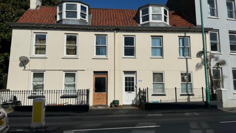 A cream house with 12 windows and two doors, with a black fence in front of it. 