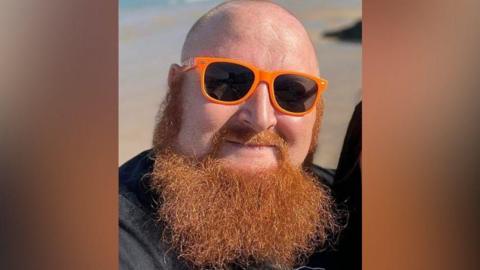 A selfie of a bald man who is wearing orange sunglasses and has a long, bushy ginger beard. 