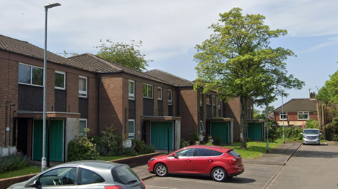 A street view image of Oakwell Grove with cars parked on the road next to terraced houses.