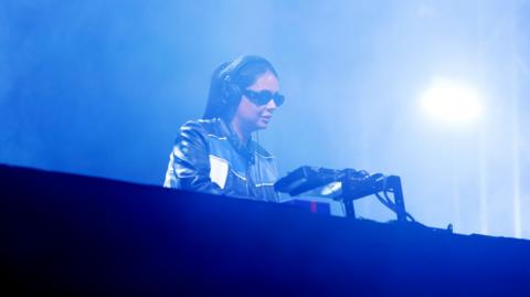 DJ Hannah Laing in a DJ booth at a nightclub with atmospheric blue lighting.