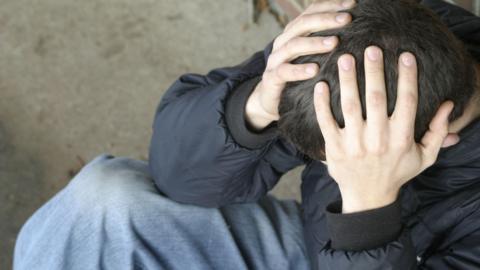 Young man sitting on the ground, looking down and with his hands on his head, seeming to be frustrated or worried.