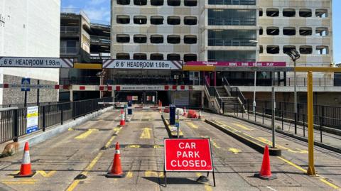 An image of the currently-closed Grafton multi-storey car park in Worthing. A closure sign can be seen alongside cones dotted across the entrance. 