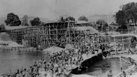 Black and white photo from showing a railway bridge being built by dozens of captured allied soldiers. 