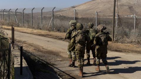 A rear view of a group of four Israeli soldiers in camouflage patroling a fence near the Lebanese border