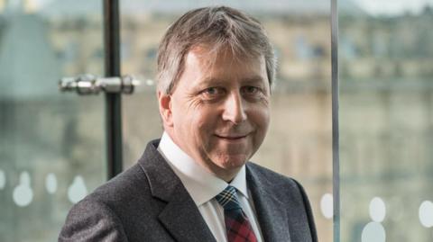 Prof Sir Peter Mathieson head and shoulders shot in a suit and tartan tie