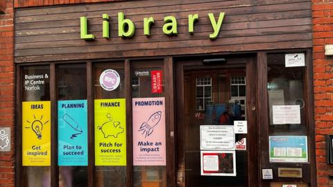 The outside of Cromer Library with posters promoting events on its windows. A sign on the door explains the library is closed.