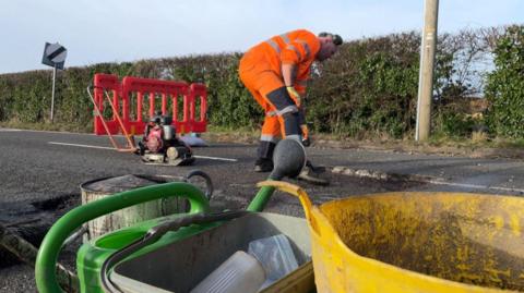 Man in orange overalls fixing a pothole in Denby, Derbyshire 