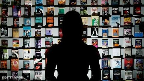 A person is silhouetted against an exhibition of James Bond book covers.