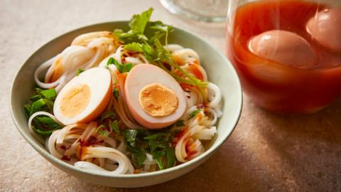 A green bowl with pickled eggs sitting on top of noodles and salad. A jar with two more eggs sitting in liquid is standing next to it.