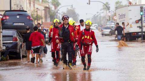 rescue workers walk down a flooded street