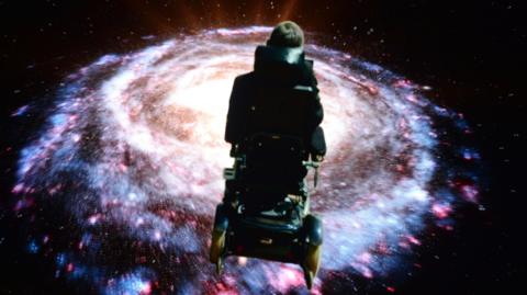 Stephen Hawking in his motorised wheelchair look down over a black hole