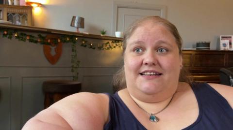 Picture of a lady wearing a blue top. There is a bar and piano in the background.