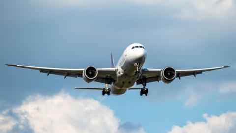 An aeroplane, viewed from the ground, is flying through a blue sky