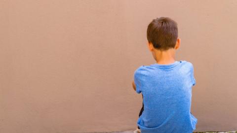 lone boy sitting on the ground behind the wall outdoor