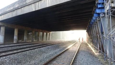 The rail bridge, which is made of grey concrete and is situated above a railway line.