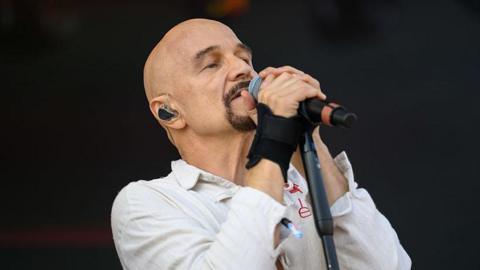 A bald man with a goatee singing into a microphone