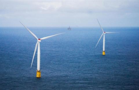 Two white wind turbines with yellow bases in a blue sea with a ship seen in the distance