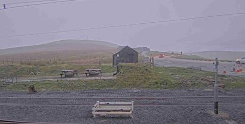 The mountain covered in fog, with a wooden bungalow and picnic benches out.