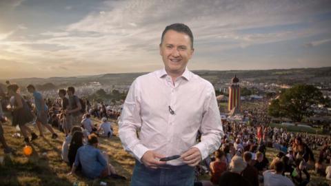Matt Taylor standing in front of a picture of a field at Glastonbury