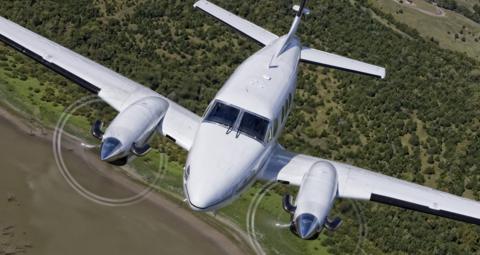 A blue and white plane.  Its propellers are moving. It is ascending. There is greenery underneath.