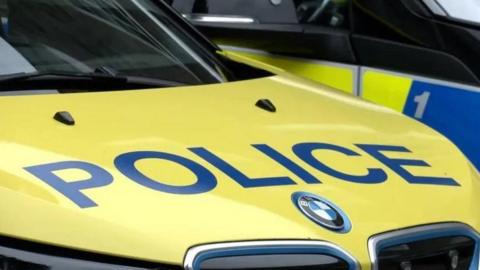 A photo which shows the bonnet of a police car. On the front of the car 'police' is written across it in blue and capital letters.