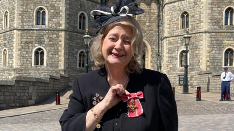 Wendy Daunt OBE standing outside Windsor Castle with her medal.