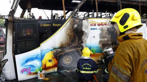 Firefighters spray water onto a burned out bus that features colourful drawings of underwater creatures.