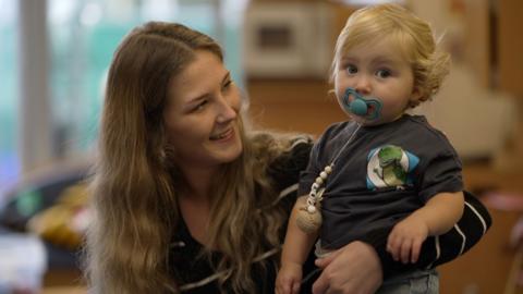 A mother smiles at the toddler she is holding in her arms