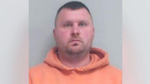 A police mugshot of Yuen Lawson looking at the camera, he is wearing an orange hoodie.