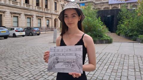 Cristiana Borg holding one of her drawings as she stands outside the Royal Academy of Arts