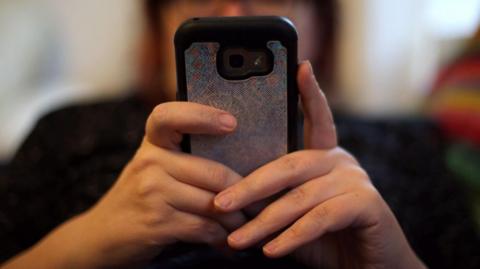 A woman on a phone. Her hands or visible but her face is blurred. She is texting or scrolling.