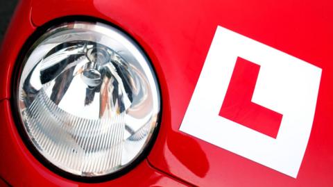 A bright red car up close with a white learner sticker on the bonnet 